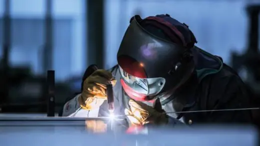 Welder in a protective helmet TIG welding a steel part