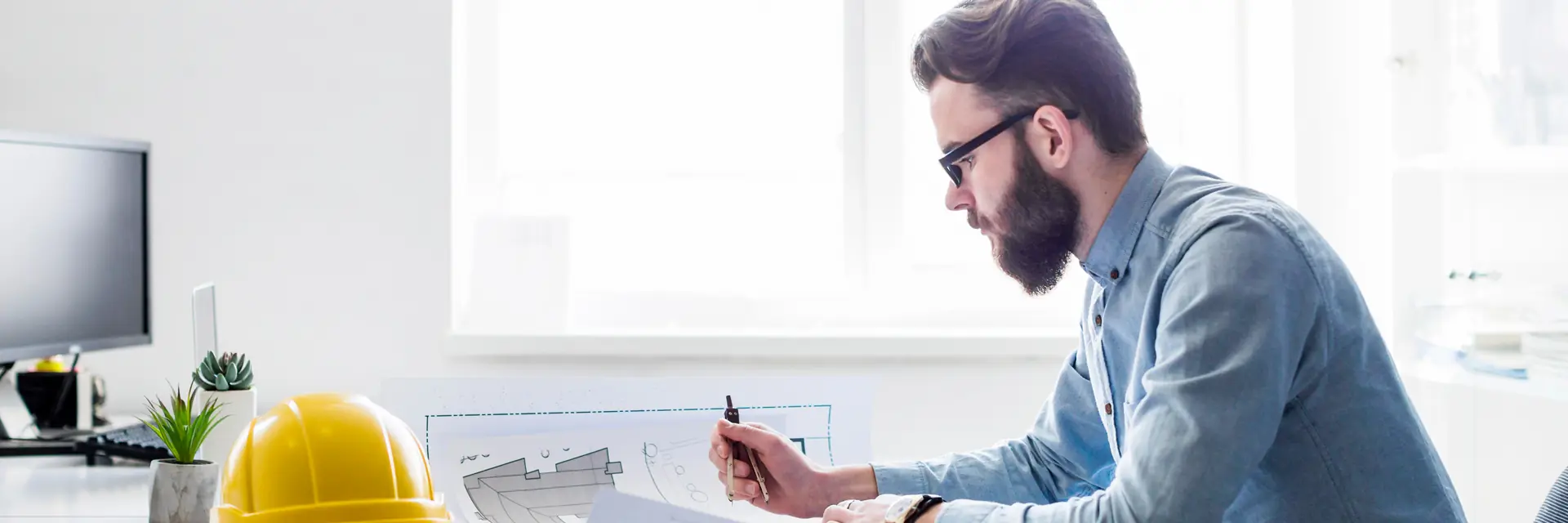 Engineer reviewing technical drawings at a desk beside a yellow hard hat