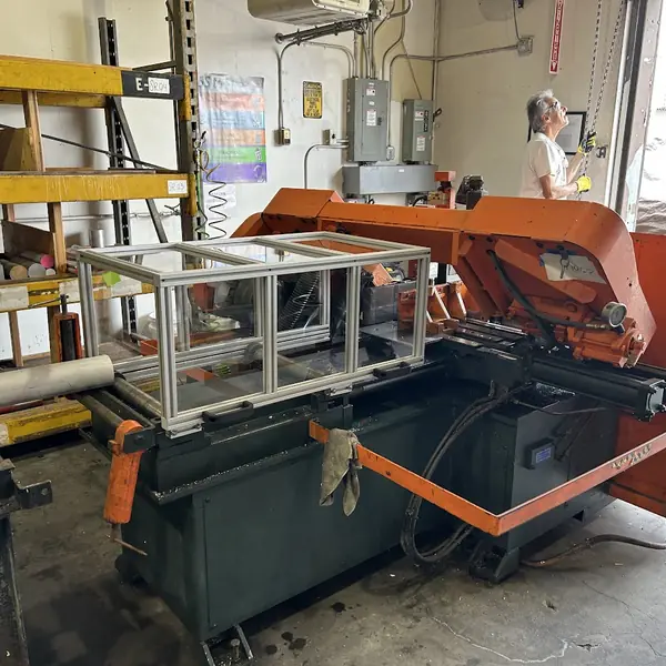 Orange horizontal band saw fitted with a clear aluminum-frame guard over the blade