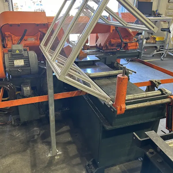 Hinged aluminum-frame guard raised open on an orange horizontal band saw