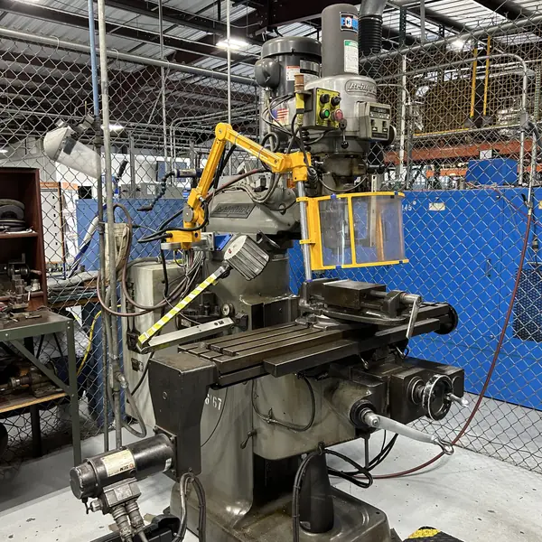 Bridgeport milling machine with a yellow articulating arm and clear spindle shield