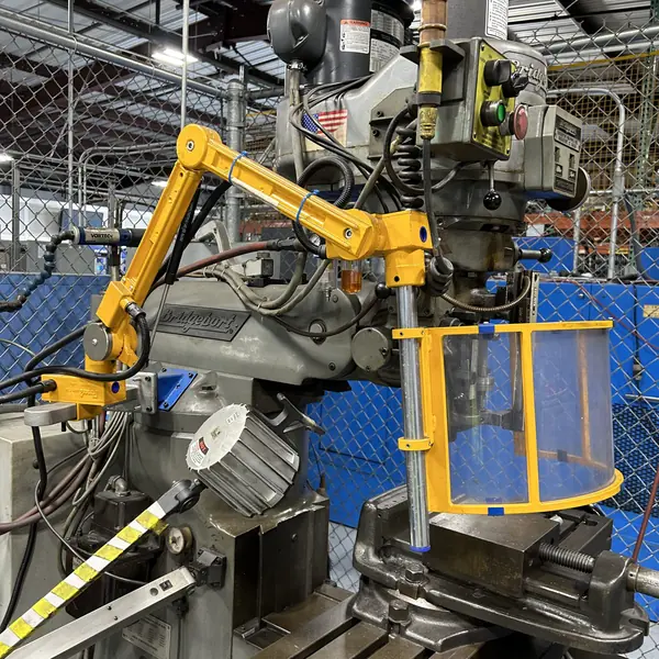 Yellow articulating arm holding a clear chip shield at the spindle of a Bridgeport mill
