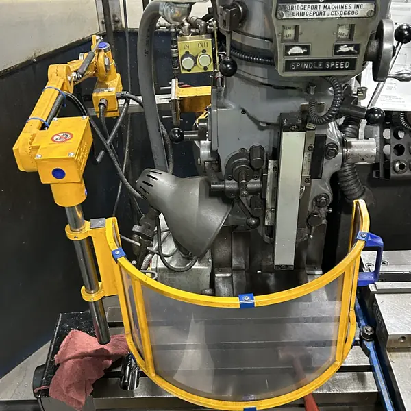 Curved clear spindle shield on a yellow arm mounted to a Bridgeport mill