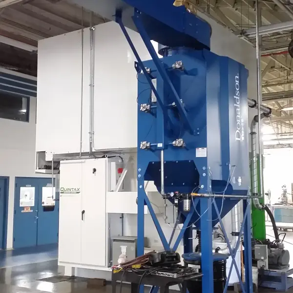 Tall blue cartridge dust collector installed beside a white booth
