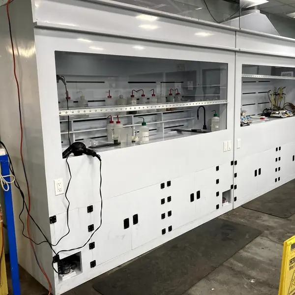 Long white polypropylene fume hood with sliding sashes and chemical bottles inside