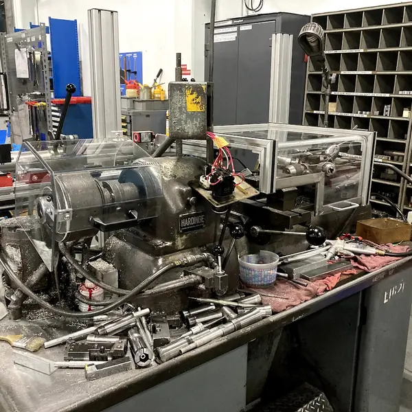 Hardinge lathe on a workbench with a clear aluminum-frame guard enclosure