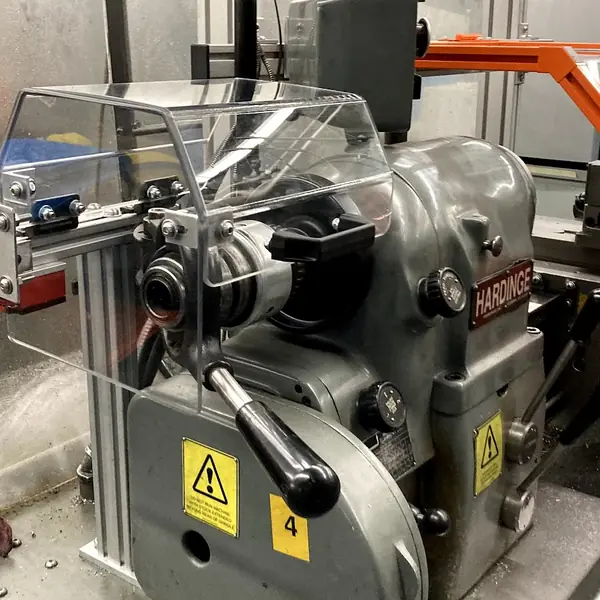 Hardinge lathe with a clear chuck shield under an orange-frame guard