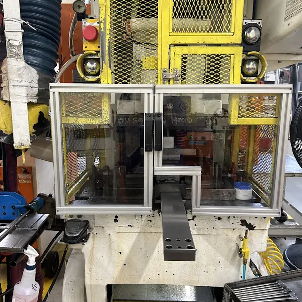 Hydraulic press with a clear aluminum-frame guard and double doors in front of the die area