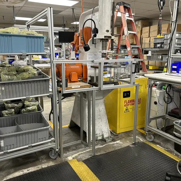 Small hydraulic press at a workstation surrounded by an aluminum-frame guard