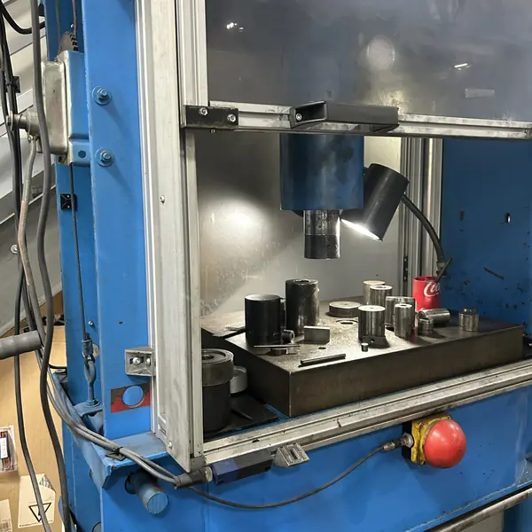 Hydraulic press ram behind a clear guard panel with a red emergency stop button