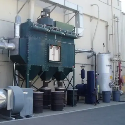 Green outdoor baghouse dust collector with collection drums and ductwork