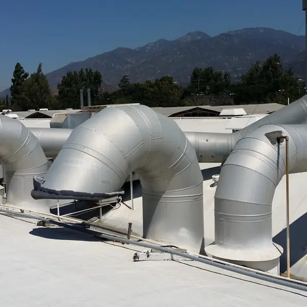 Large galvanized exhaust ductwork elbows on a rooftop with mountains behind